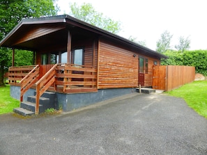 A wooden cabin with a porch, a staircase, and a paved driveway.