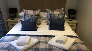 A neatly made bed with plaid bedding, two decorative pillows, and two folded towels.
