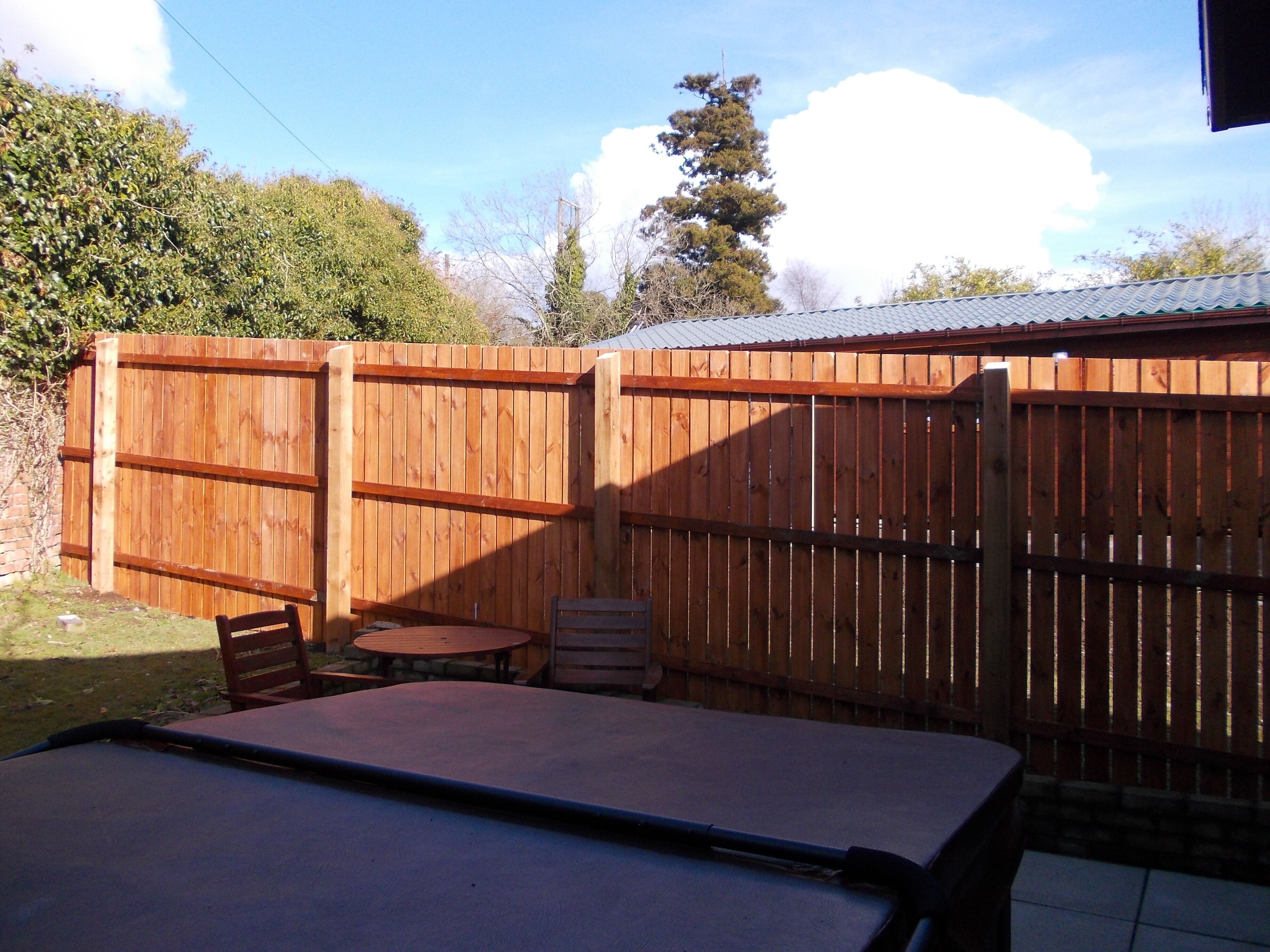 A patio area with a wooden fence, a table, and two chairs.
