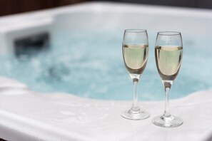 Two champagne flutes on a white surface with a hot tub in the background.