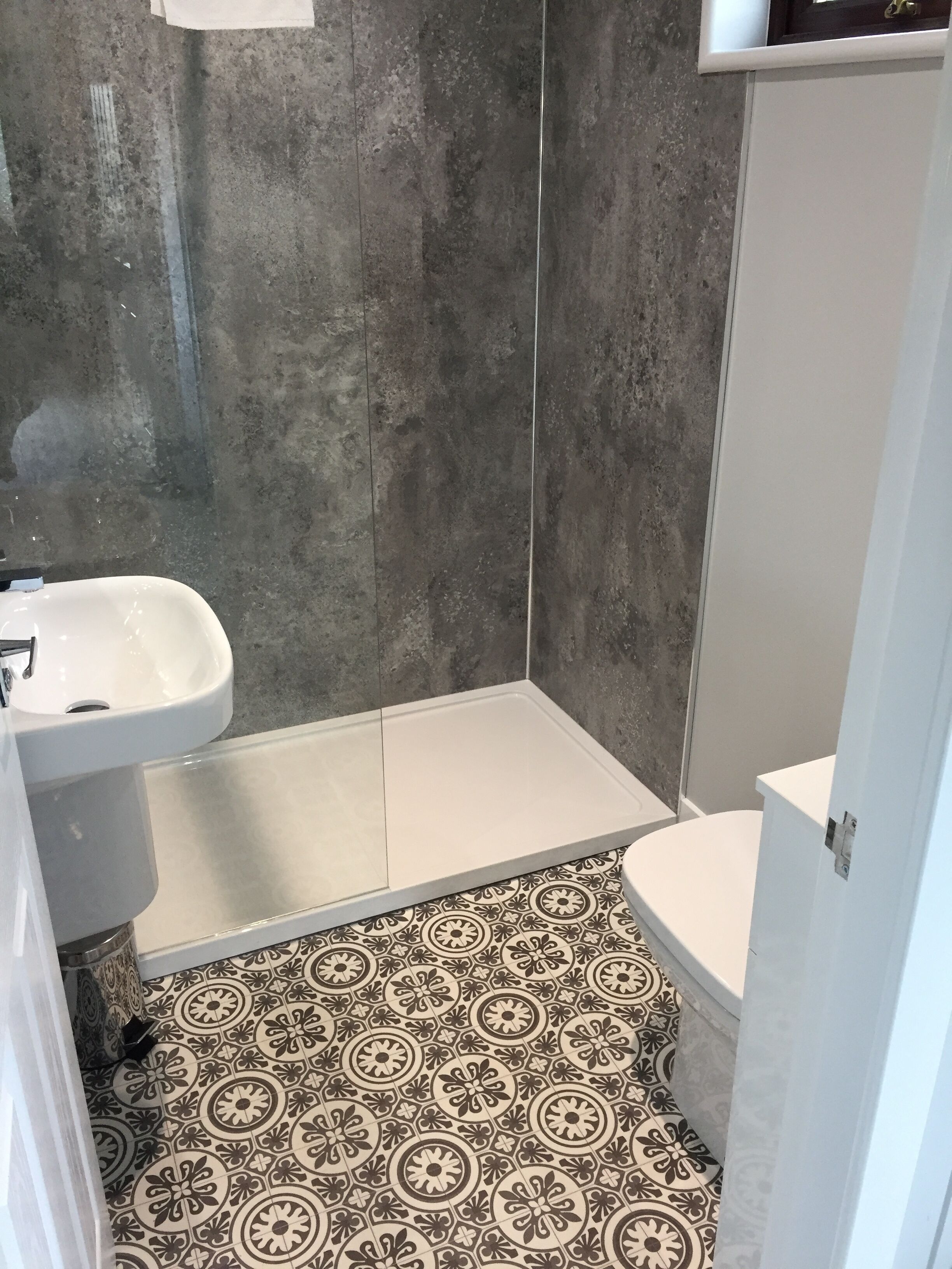 A bathroom with a white sink, toilet, and shower area. The floor has patterned tiles.
