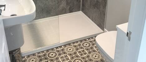 A bathroom with a white sink, toilet, and shower area. The floor has patterned tiles.