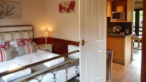 A bedroom with a bed, bedside table, lamp, and a view into the kitchen.