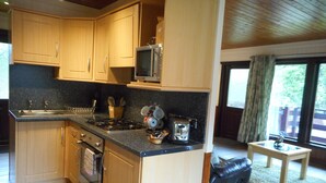 A kitchen with wooden cabinets, a stove, a microwave, and a sink. There is a window with a view of trees outside.