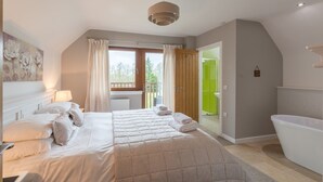 A bedroom with a large bed, a bathroom with a bathtub, and a balcony with a view of trees. - Lord Galloway 32 (H 2016) 82334 (Newton Stewart)