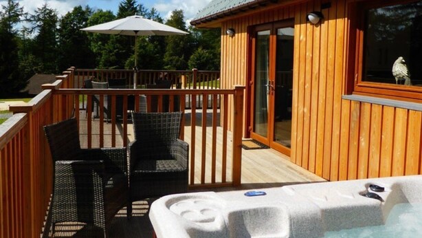 A wooden deck with outdoor furniture, a hot tub, and a covered area with an umbrella. - Lord Galloway 32 (H 2016) 82334 (Newton Stewart)