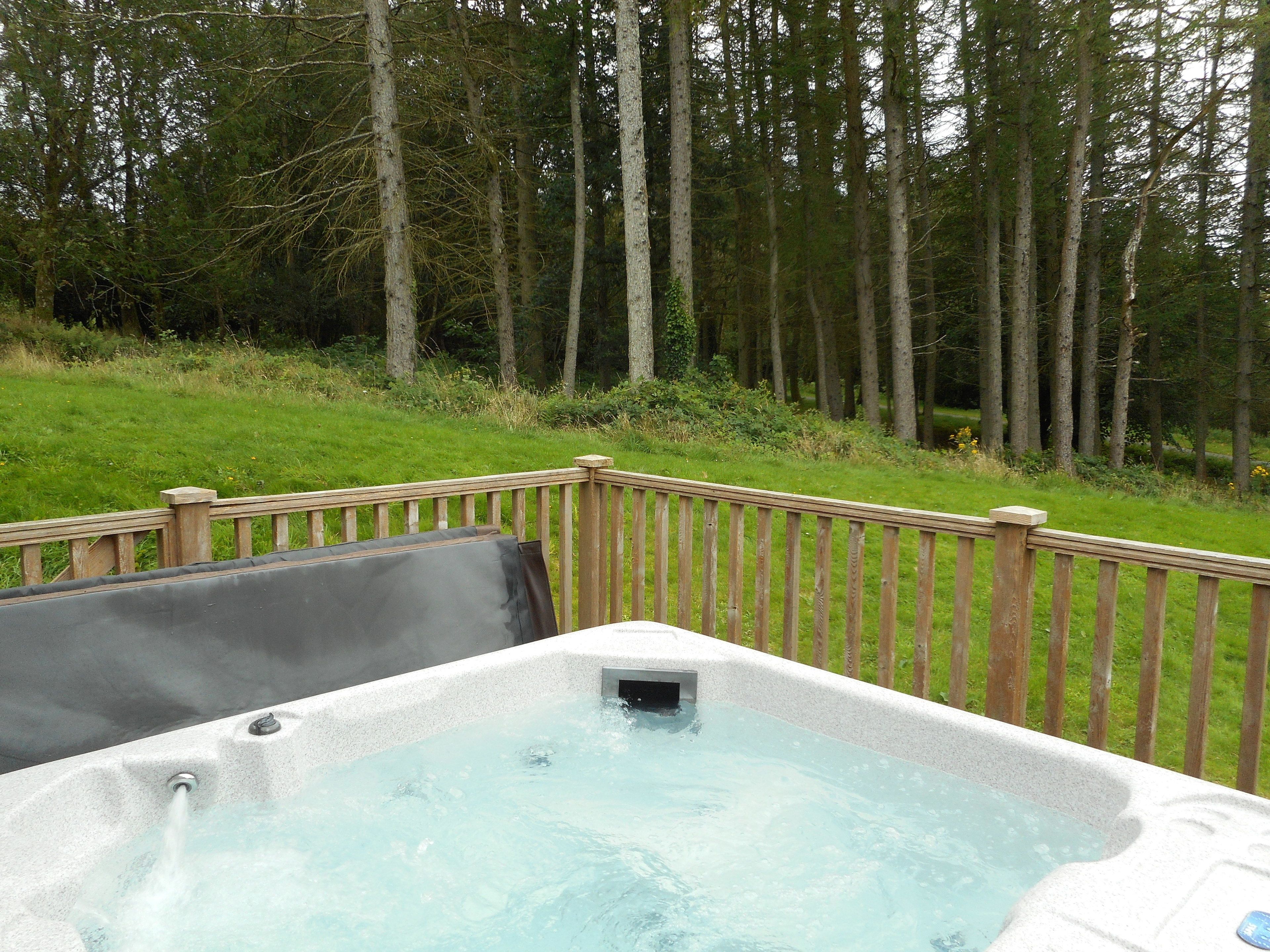 A hot tub with a wooden deck and a grassy area with trees in the background.