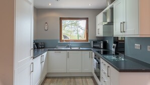 A modern kitchen with white cabinets, a window with a view of trees, and a microwave. - Lord Galloway 32 (H 2016) 82334 (Newton Stewart)