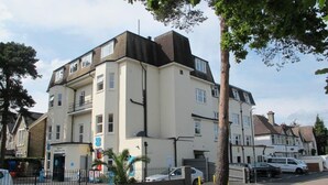 A multi-story building with a flat roof, a gated entrance, and a visible sign for a business. - Flat 8 Palm Court (Bournemouth)