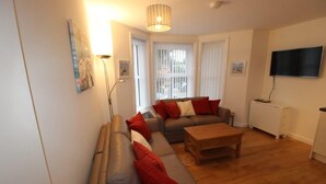 A living room with a sofa set, a coffee table, a TV, and a radiator. - Flat 8 Palm Court (Bournemouth)