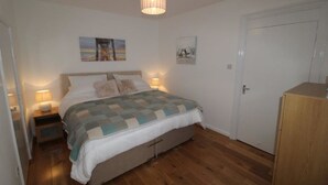 A bedroom with a bed, two bedside tables with lamps, a wooden wardrobe, and two wall-mounted pictures. - Flat 8 Palm Court (Bournemouth)