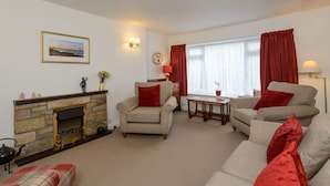 A living room with a fireplace, two armchairs, a sofa, a table, and a window with curtains. - Swifts Cottage (Tranent)