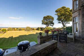 A patio with a barbecue grill, outdoor seating, and a view of the sea.