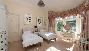 A bedroom with two beds, a dresser, a vanity with a mirror, and artwork on the walls.