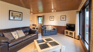 A cozy living room with a brown leather sofa, a blue sofa, a coffee table, and a TV on a wooden stand. - Bluebell Lodge 3 with Hot Tub (Newton Stewart)