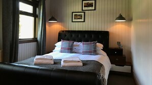 A neatly made bed with plaid pillows and folded towels, a dark headboard, and two bedside lamps. - Bluebell Lodge 3 with Hot Tub (Newton Stewart)
