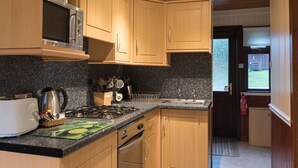 A kitchen with wooden cabinets, a microwave, a gas stove, and a sink. - Bluebell Lodge 3 with Hot Tub (Newton Stewart)
