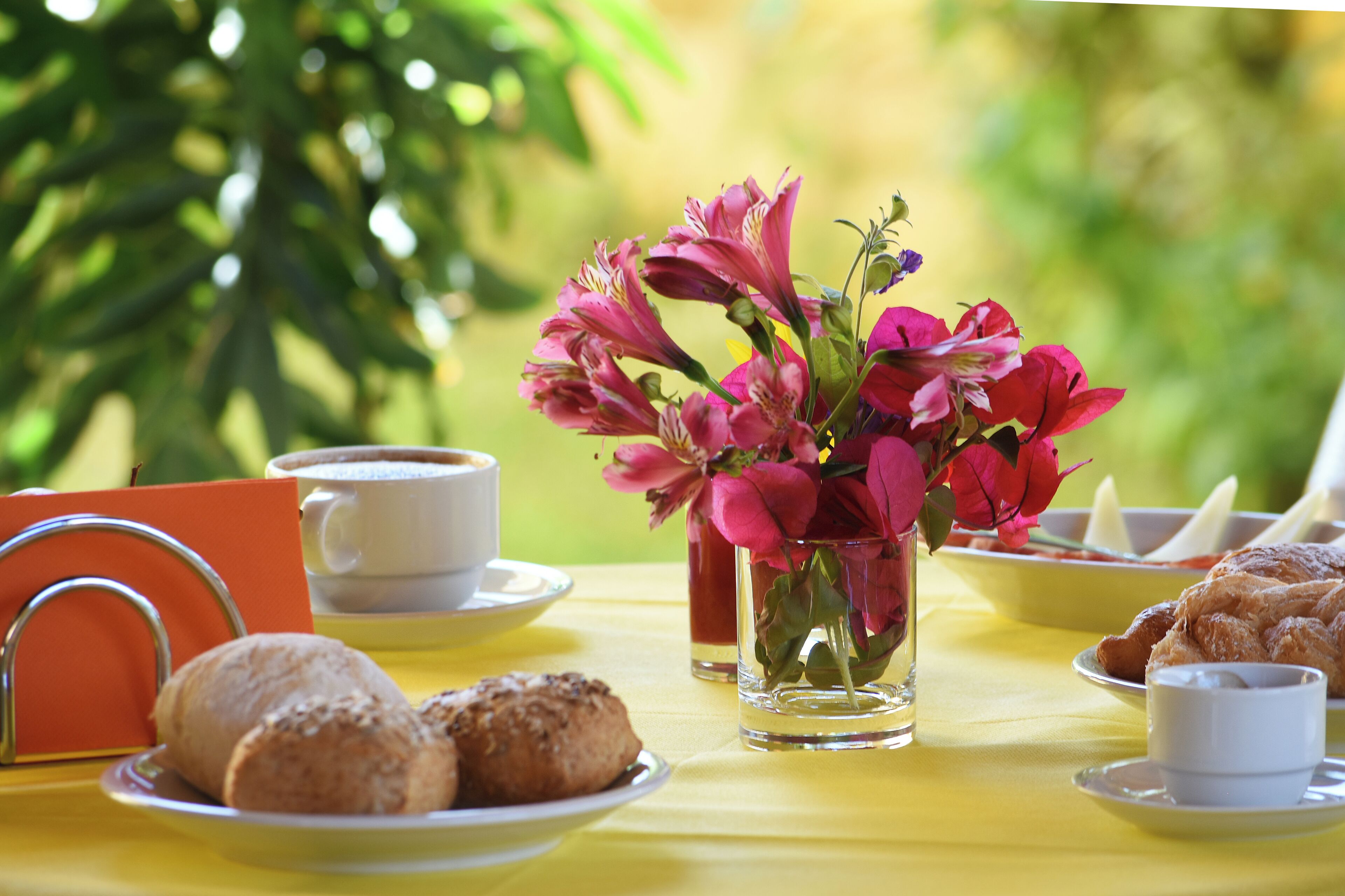 A table set with pastries, a cup of coffee, a vase of flowers, and a teapot.