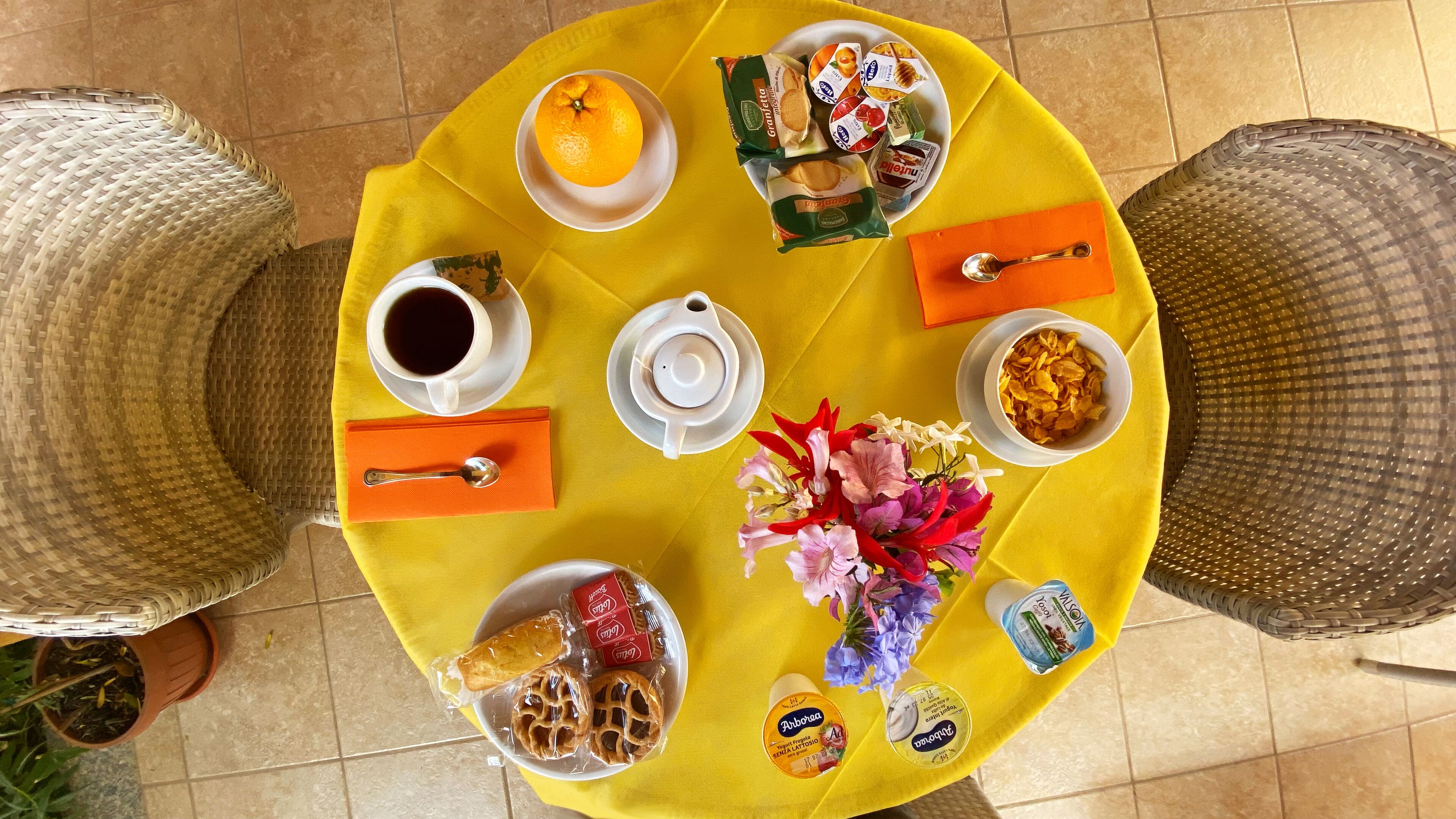 A round table with a yellow tablecloth, various food items, a cup of coffee, and a teapot.
