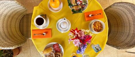 A round table with a yellow tablecloth, various food items, a cup of coffee, and a teapot.