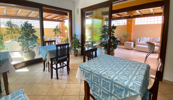 A dining area with a table and chairs, potted plants, and a view of an outdoor seating area. - Il Girasole Hotel (Villasimius)