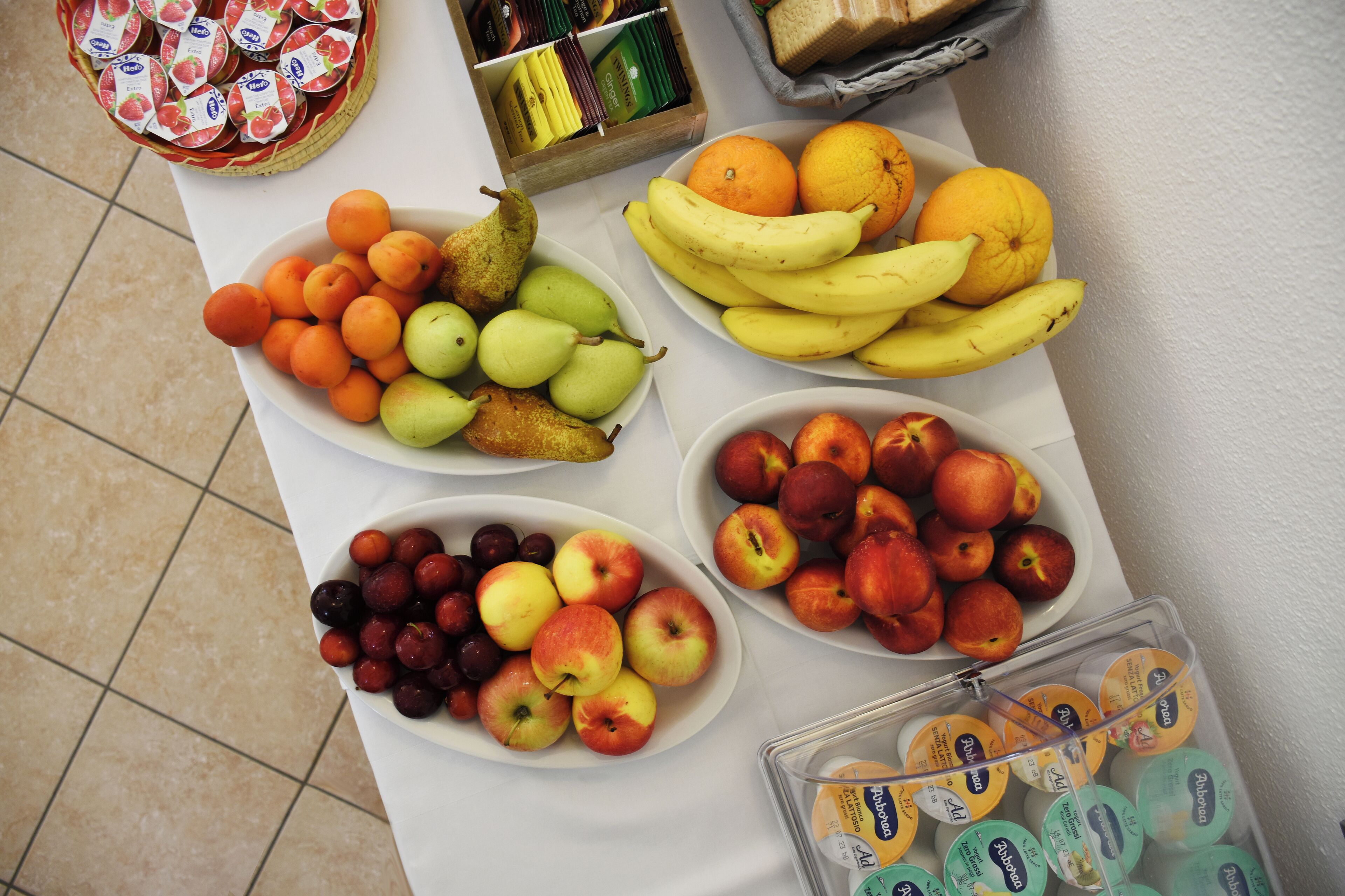 A table with various fruits and a basket of yogurt cups.