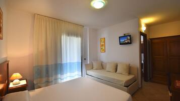 Habitación de hotel con cama, sofá, mesita de noche con lámpara, cortina e imagen colgada en la pared.