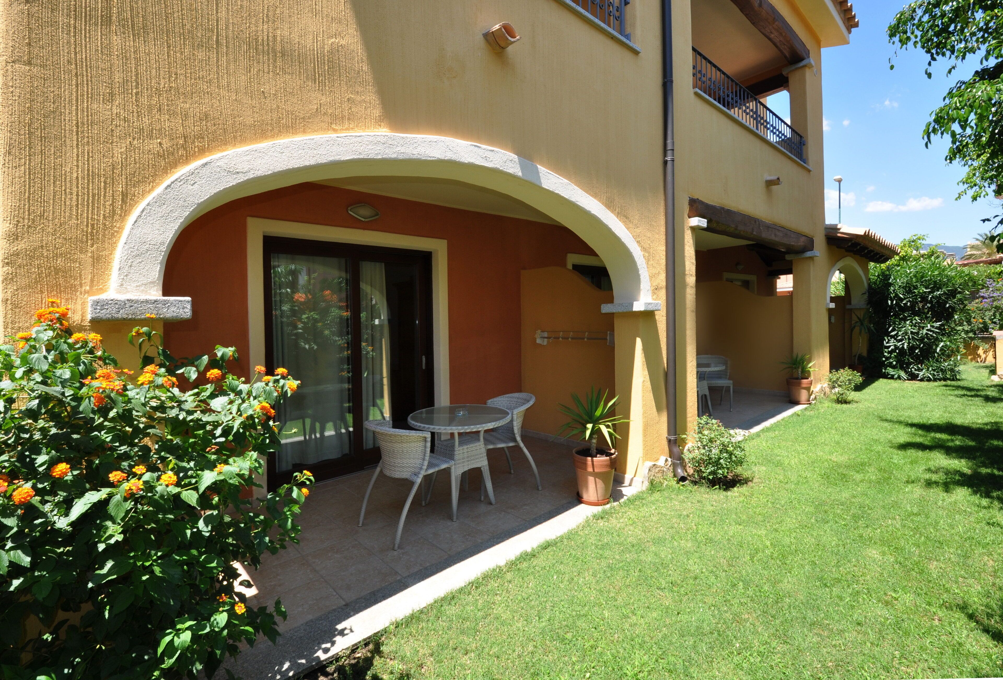 A two-story building with a covered patio area featuring a table and chairs, a potted plant, and a small garden.