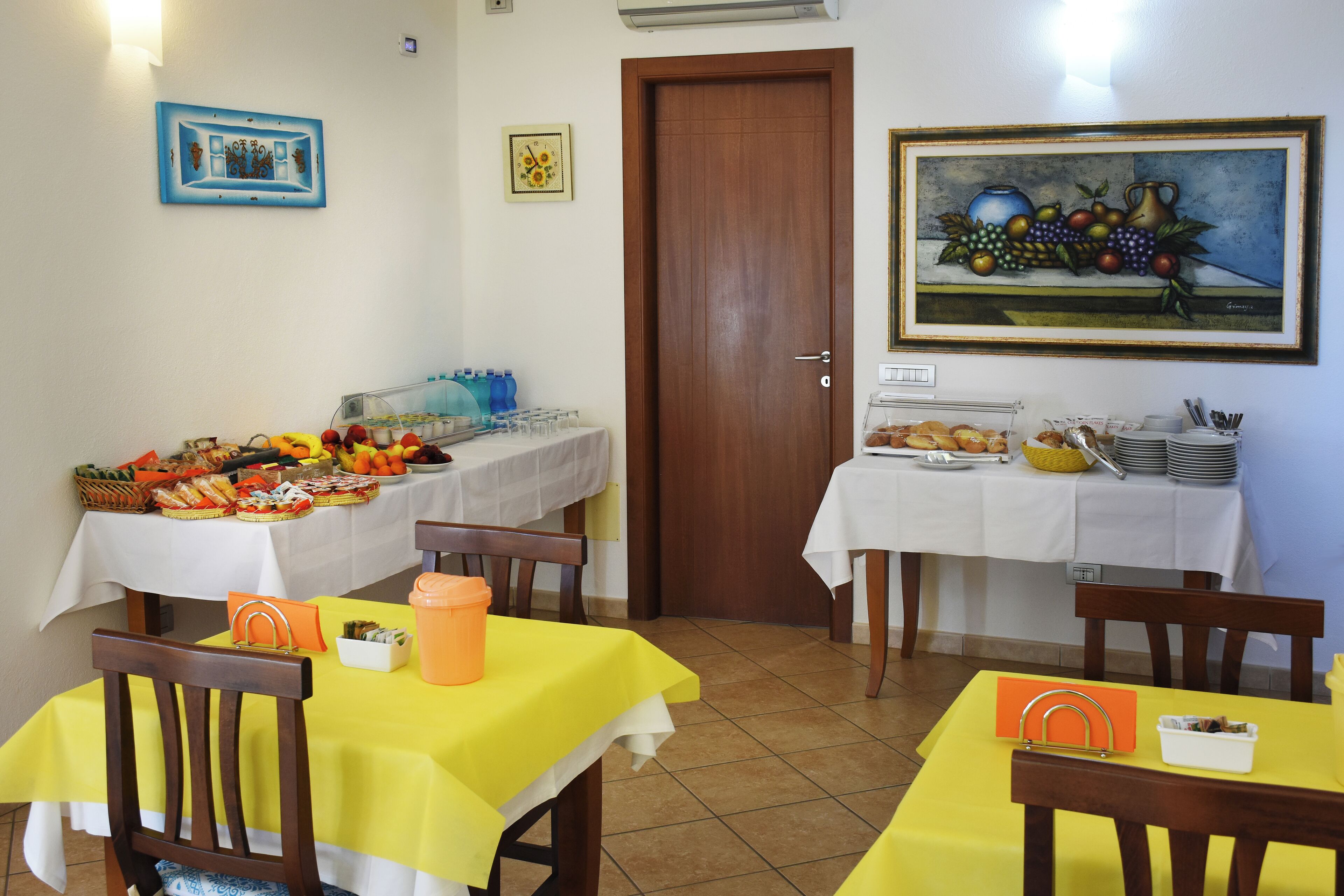 A dining area with tables set for breakfast, featuring a variety of food items and a painting on the wall.