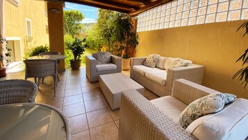 Un patio techado con mobiliario de mimbre, una mesa de vidrio y plantas en macetas.
