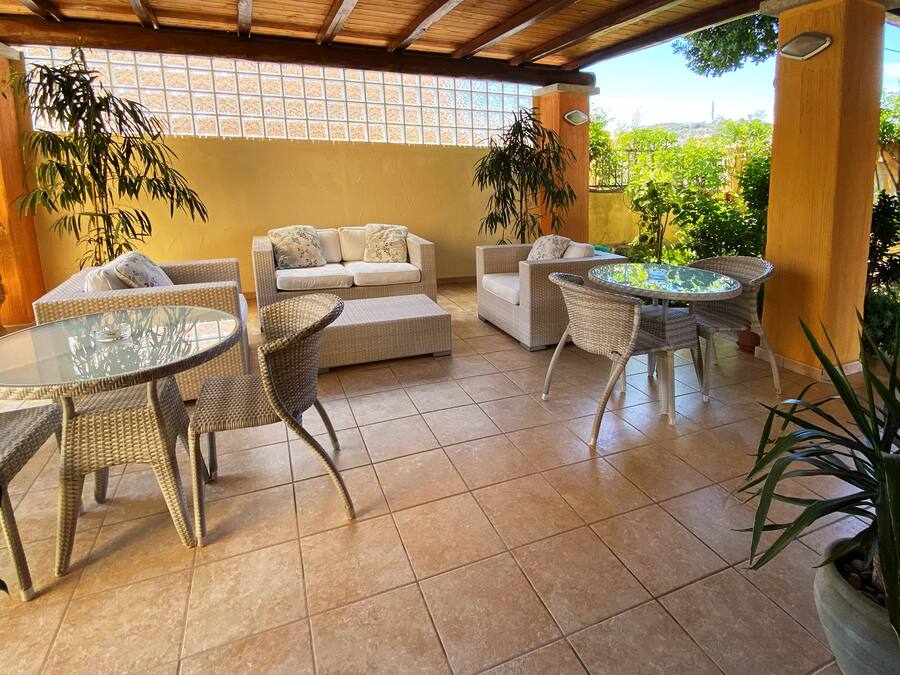 A covered patio area with wicker furniture, a glass table, and potted plants.