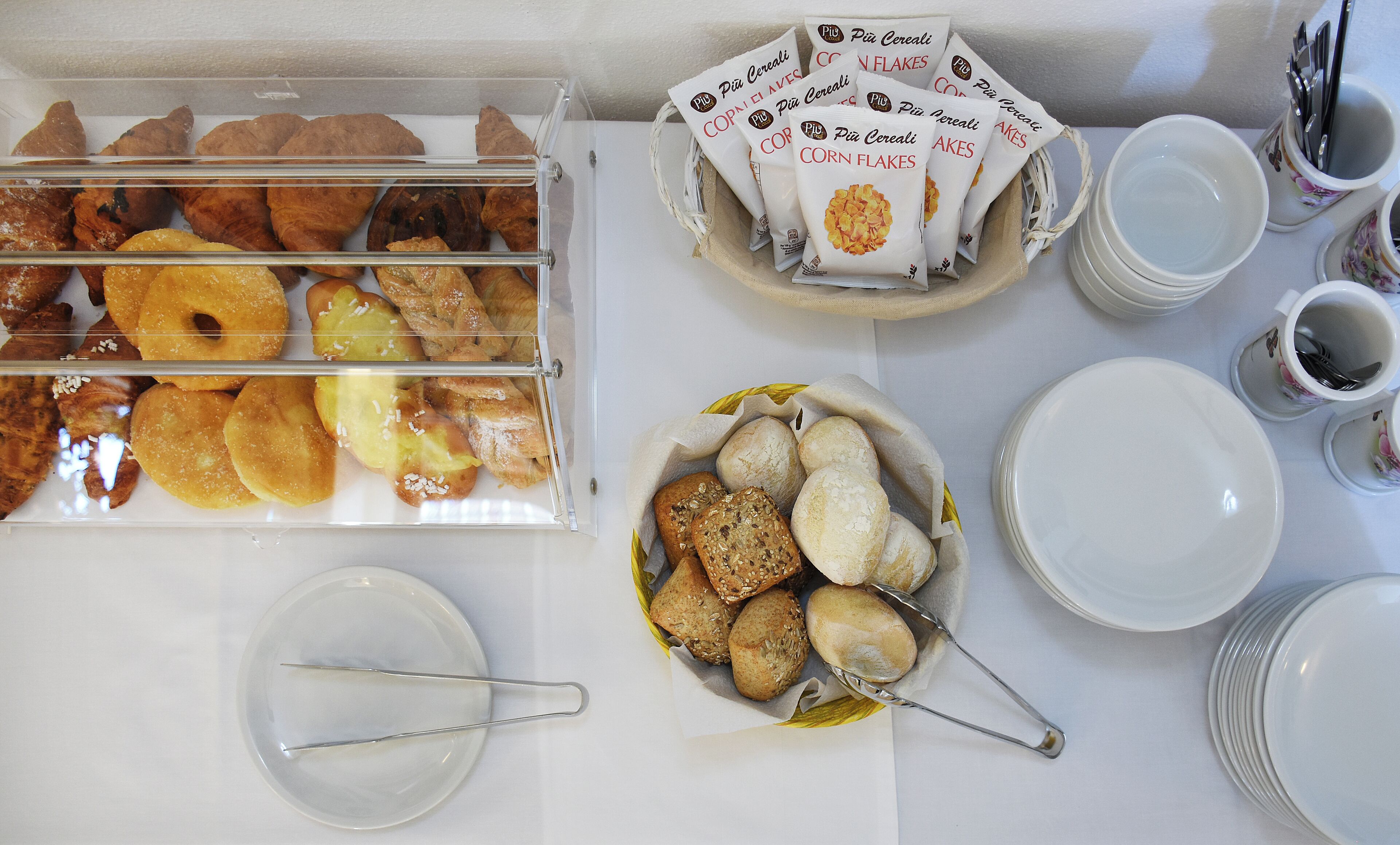 Un bufé de desayuno con diversos pasteles y pan, acompañado de platos, tazas y cubiertos.