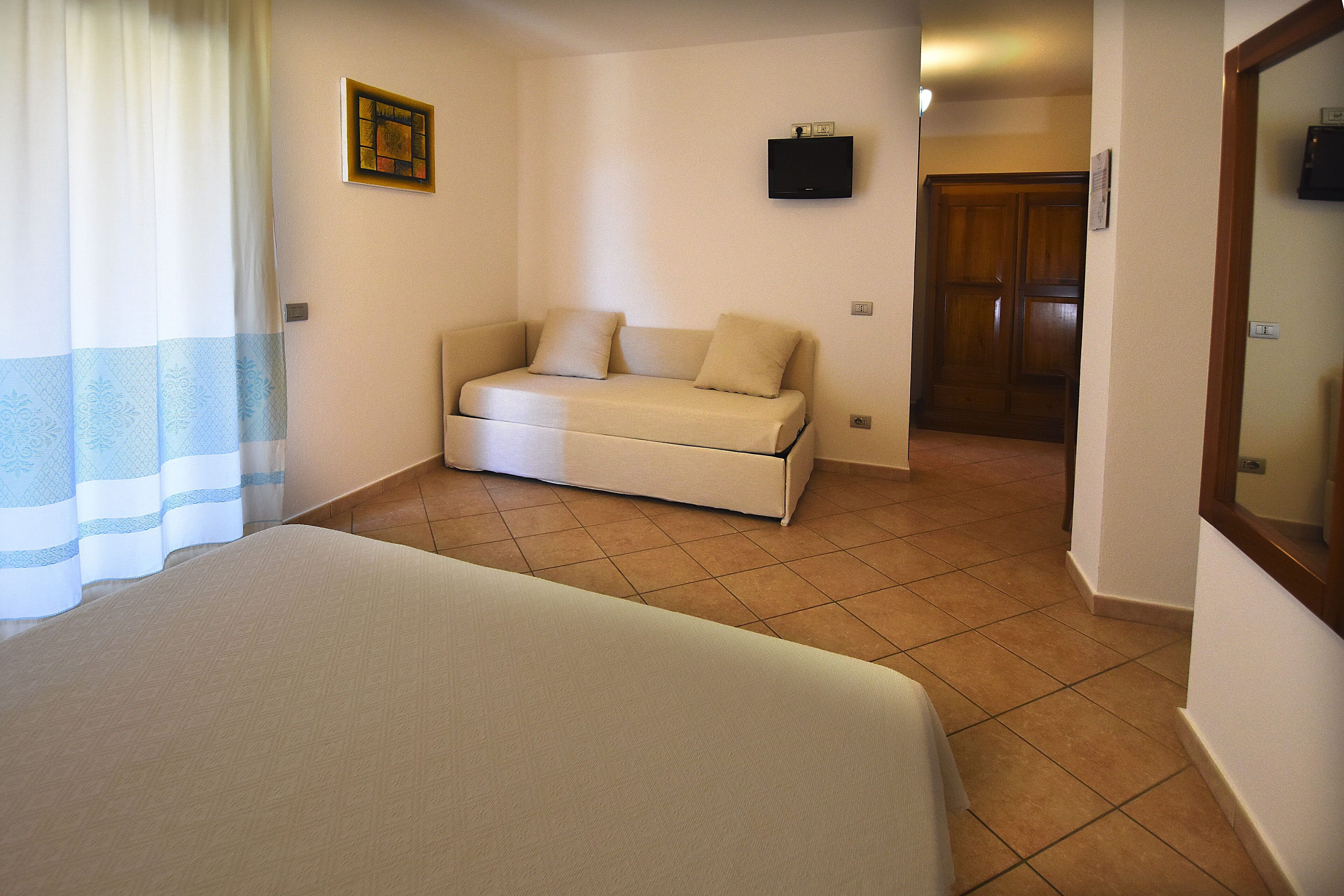 Ein Schlafzimmer mit Bett, einer Schlafcouch, einem Fernseher an der Wand und einer Holztür.