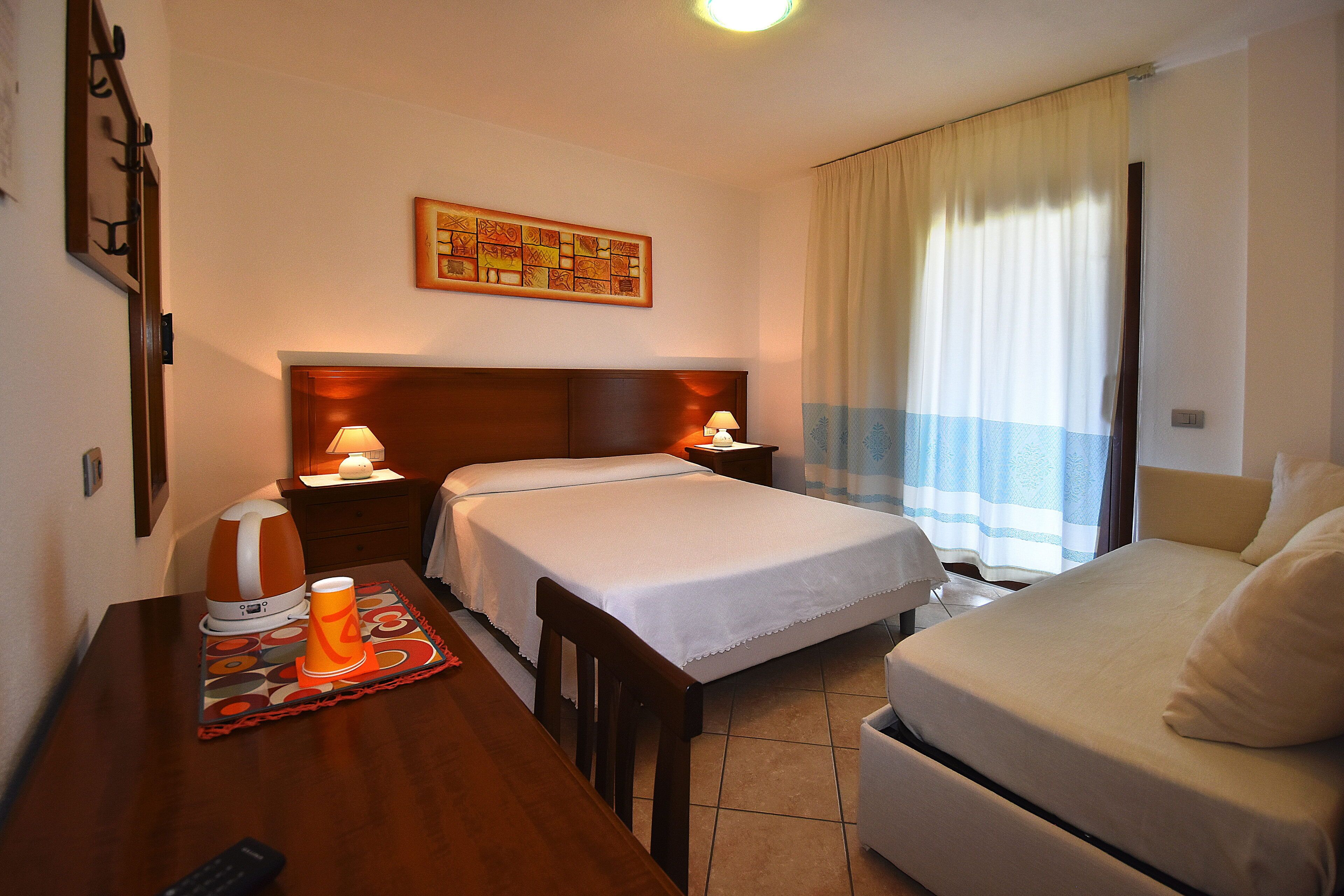 A hotel room with two beds, a desk with a lamp, a coffee maker, and a painting on the wall.