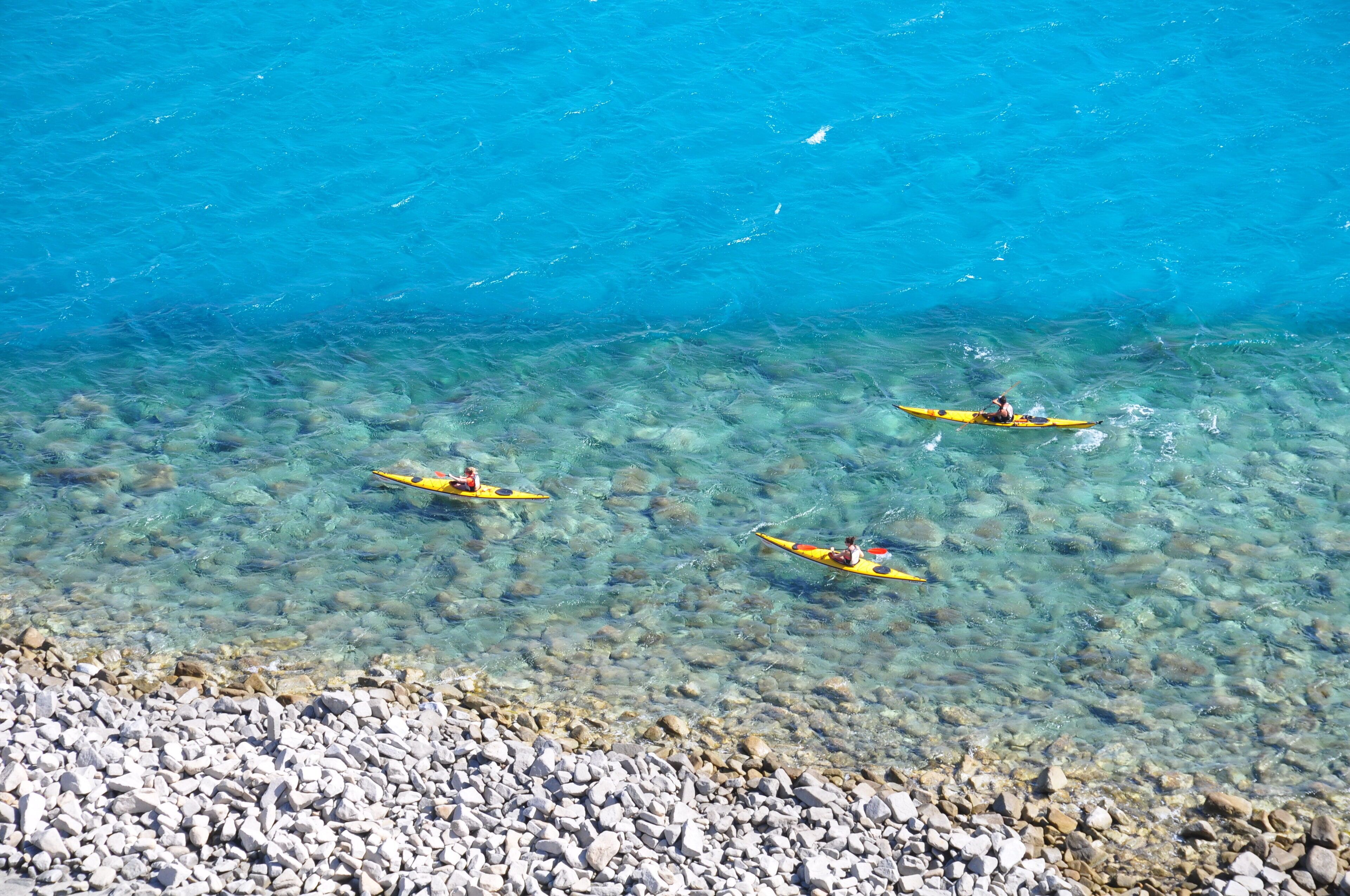 Kayakers on a clear blue sea with a rocky shore in the foreground.