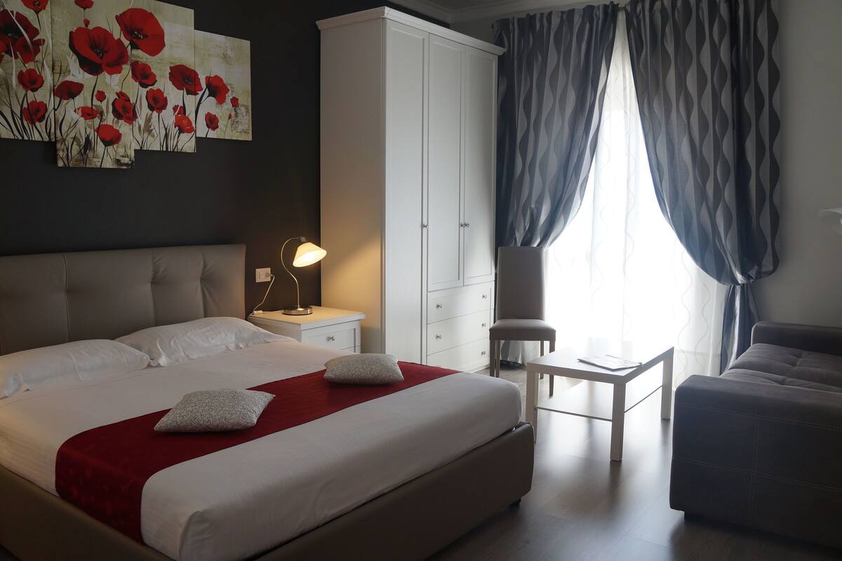 A hotel room with a large bed, a wardrobe, a desk, and a chair.
