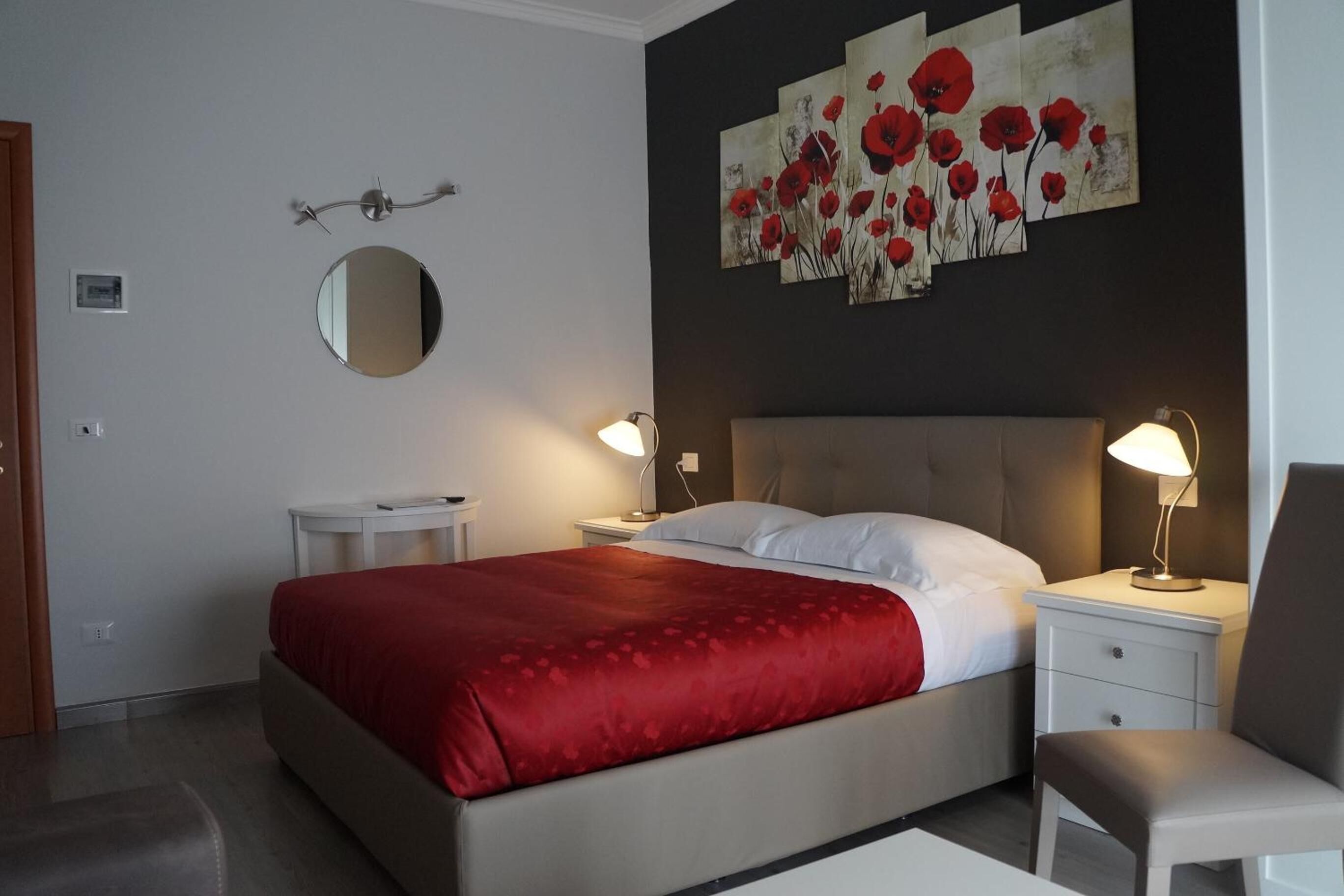Habitación de hotel con una cama grande, dos mesitas de noche, una silla, un espejo redondo y una obra de arte en la pared.