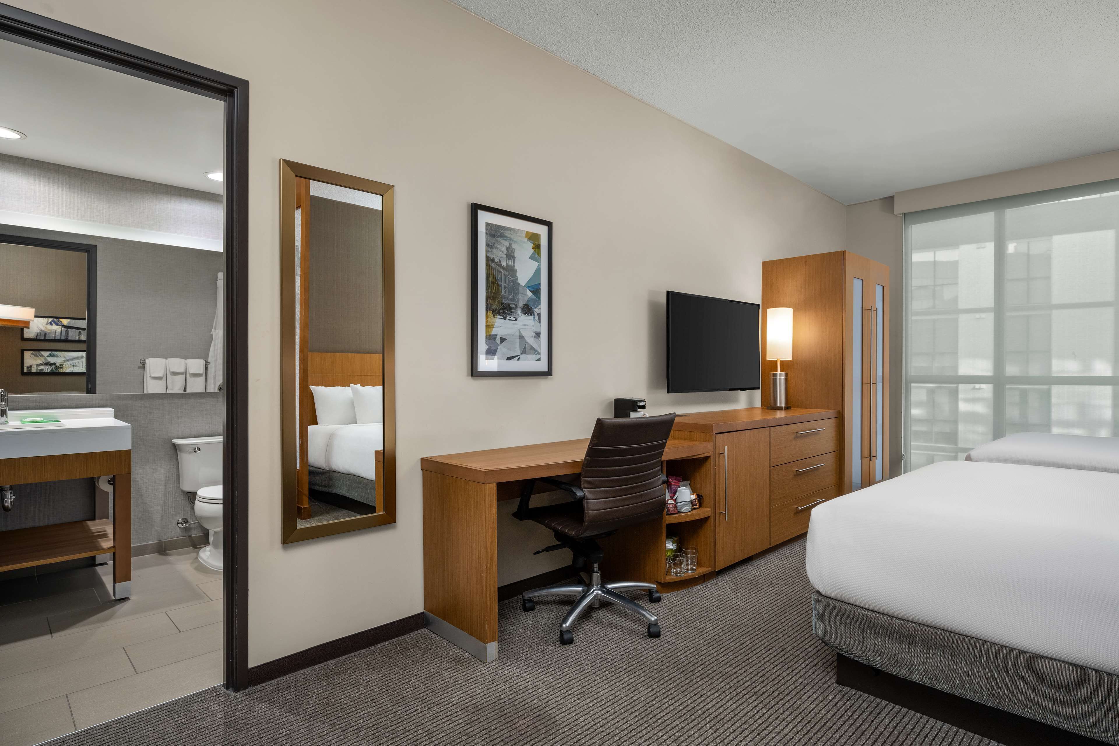 A hotel room with a bed, desk, chair, TV, and a bathroom with a toilet and sink.
