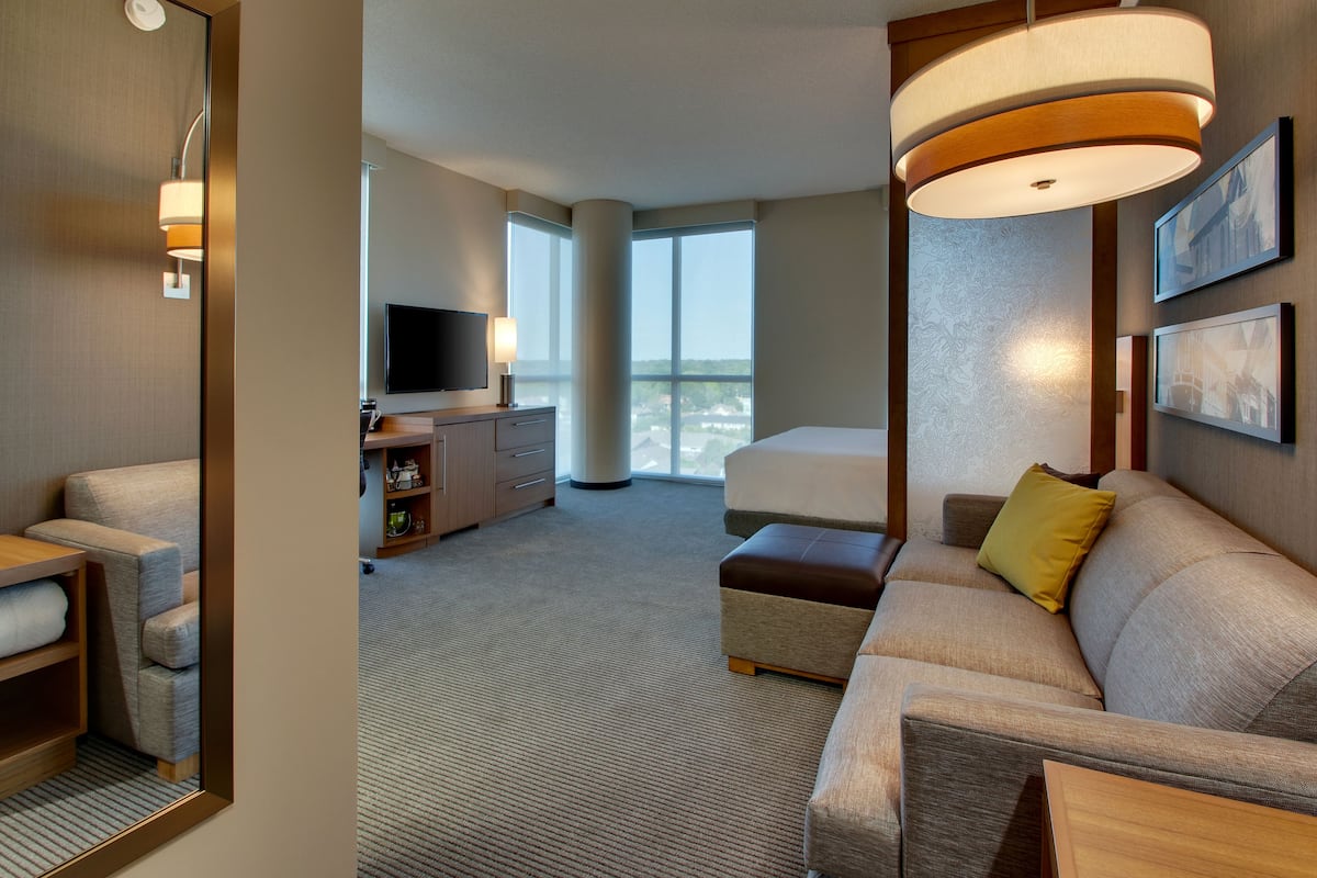 Une chambre d’hôtel avec une grande fenêtre, un canapé, une télévision et un bureau avec une lampe.
