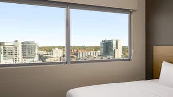 Habitación de hotel con un ventanal grande que ofrece vistas a la ciudad, una cama bien hecha y un cabecero moderno.