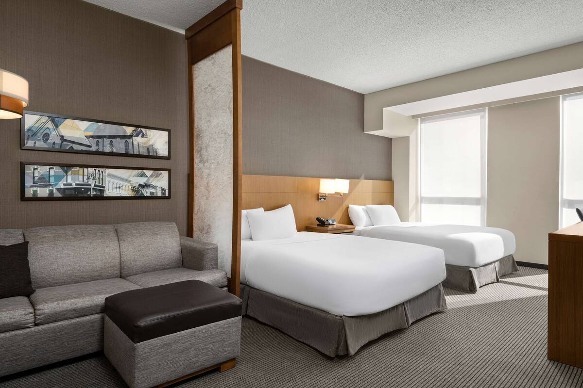 Une chambre d’hôtel avec un canapé, deux lits, un bureau et des œuvres d’art au mur.