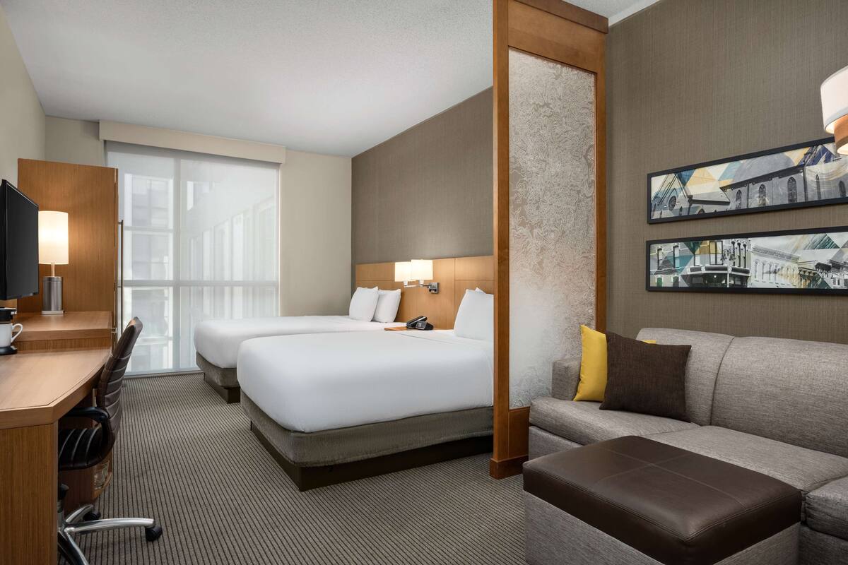 Une chambre d’hôtel avec deux lits, un bureau avec une chaise, un canapé et un téléviseur.