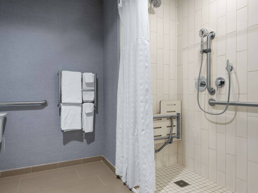 A bathroom with a toilet, a towel rack with towels, a shower with a handheld showerhead, and a grab bar.