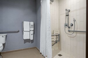 Un baño con inodoro, toallero con toallas, ducha con cabezal de ducha manual y barra de apoyo.