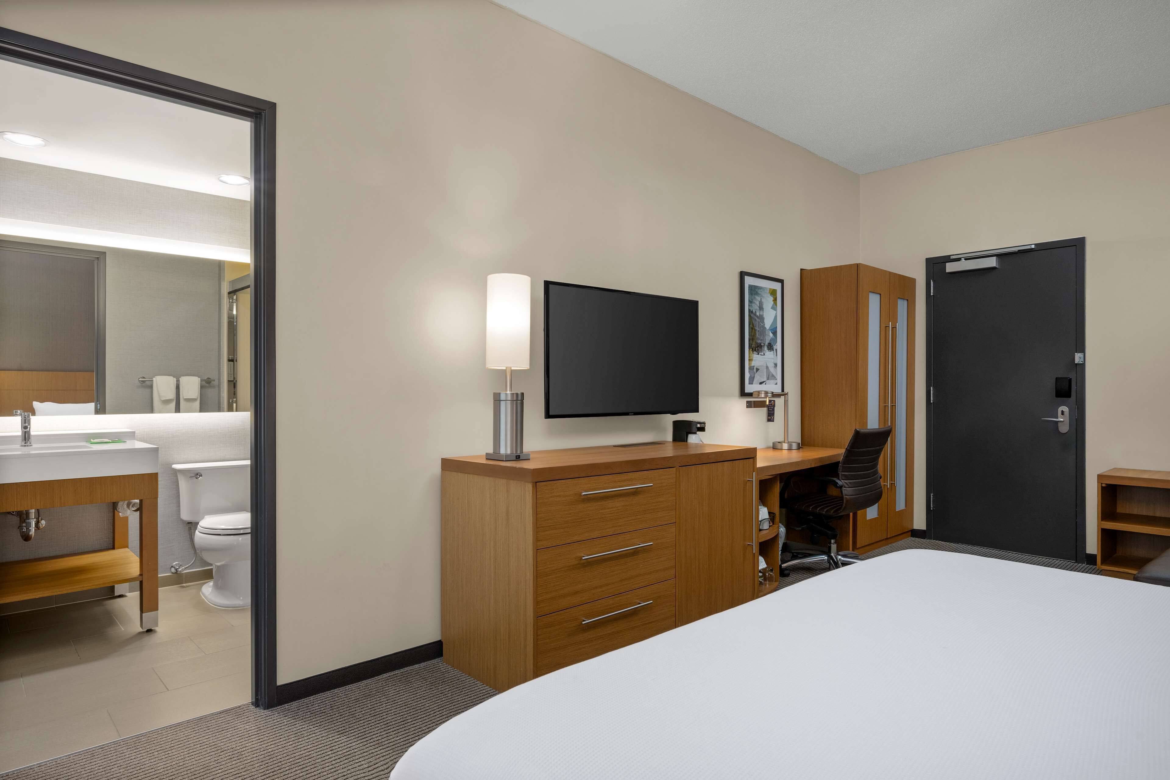A hotel room with a bed, a desk with a chair, a TV, a wardrobe, and a bathroom with a toilet and sink.