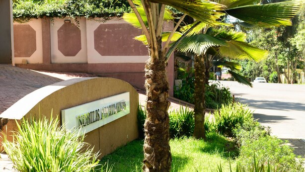 A well-maintained garden with a palm tree, a sign reading "NOBLES PARKING," and a paved walkway. - Nobilis Apartments (Kigali)