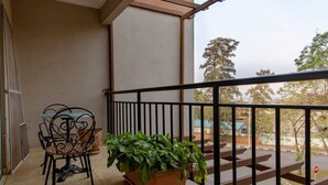 A balcony with a table and chairs, a potted plant, and a view of the street and trees. - Nobilis Apartments (Kigali)