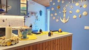 A kitchen with wooden cabinets, a blue wall with sea-themed decorations, and a wooden ceiling. - Casa Diana (Giardini Naxos)