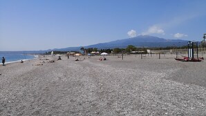 A pebbled beach with people sunbathing and a mountain in the background. - Casa Diana (Giardini Naxos)