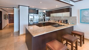 A modern kitchen with a granite countertop, stainless steel appliances, and wooden stools. - Coral Cove 11 by Altman (Paynes Bay)